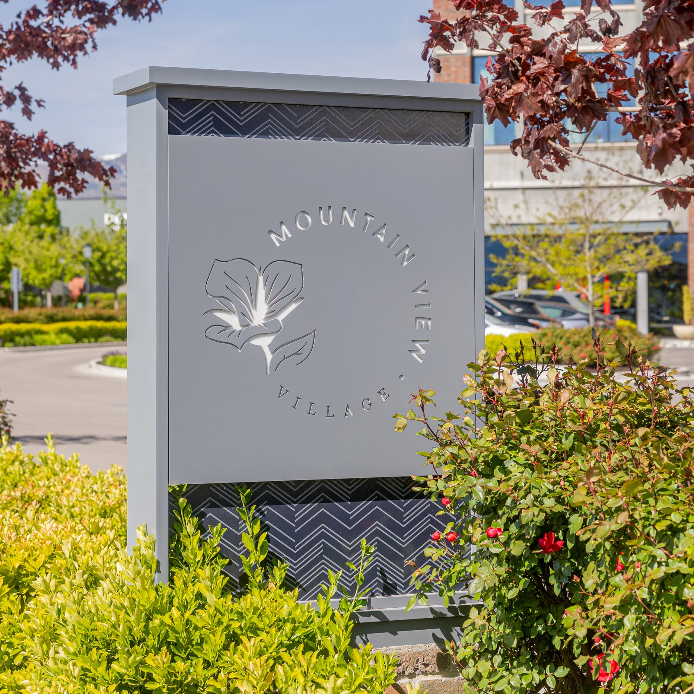 Gray monument sign with an etched sego lily emblem and "Mountain View Village" logo, set among landscaped hedges and roses at the Riverton, Utah center — environmental graphic design and monument signage by RSM Design.
