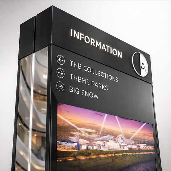 Interior wayfinding directory pylon sign at American Dream mall in East Rutherford, New Jersey, featuring directional listings for The Collections, Theme Parks, and Big Snow, an integrated digital display screen showing an aerial rendering of the complex, and the American Dream logo medallion on a matte black cabinet — showcasing RSM Design's wayfinding signage design, digital integration and interactive solutions, and master sign program for a large-scale mixed-use retail and entertainment destination.
