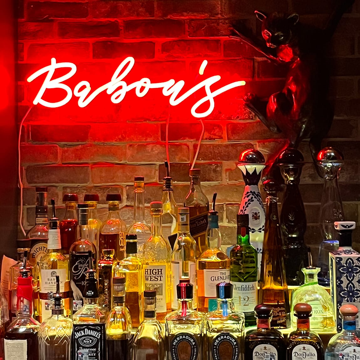 Red neon "Baboa's" script sign above a bar shelf lined with liquor bottles at The Swexan Hotel - environmental graphic design by RSM Design