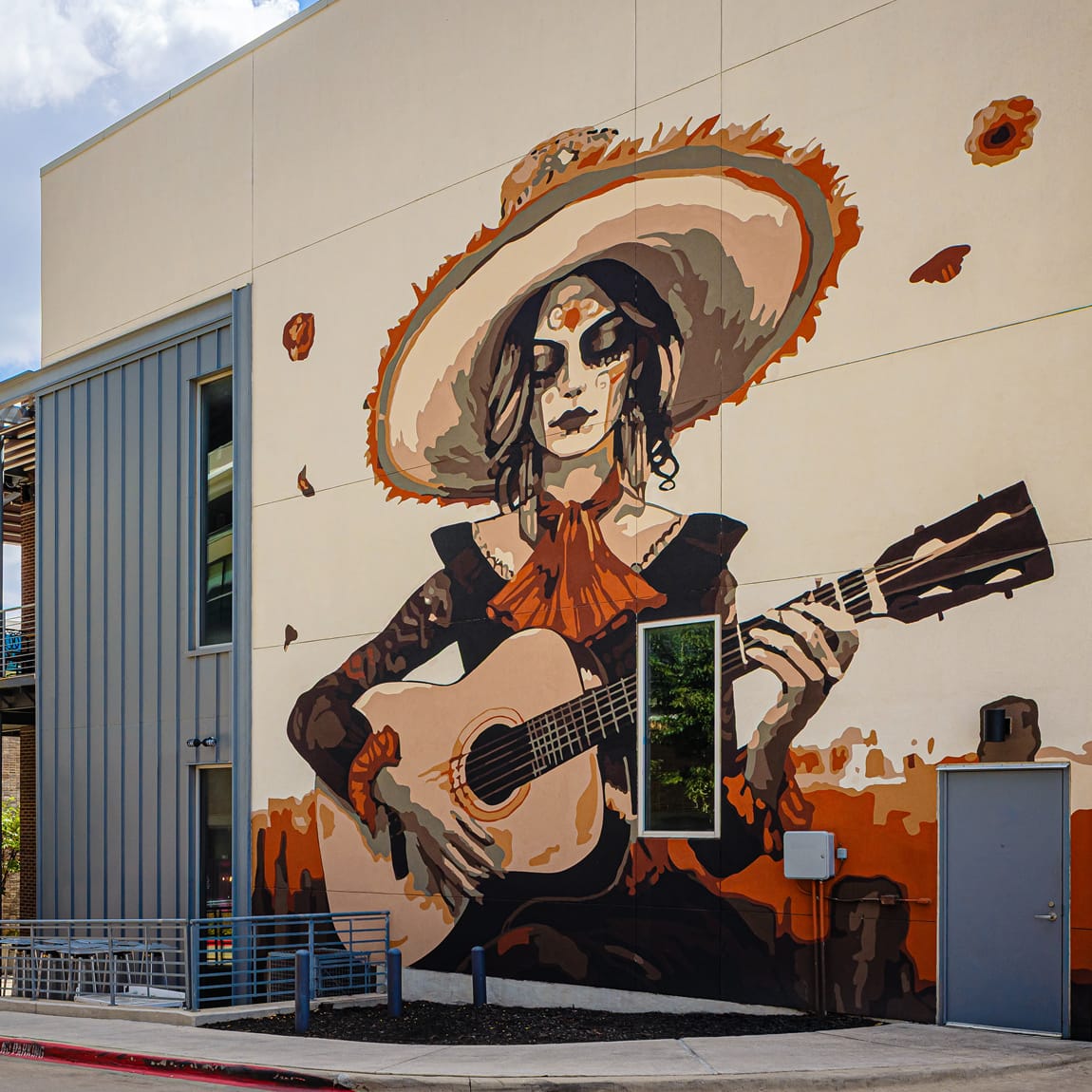 ALT TEXT:
Large-scale exterior building mural of a Day of the Dead guitarist figure with sombrero at Toyota Music Factory mixed-use entertainment district in Irving, Texas — RSM Design public art, murals, experiential graphics, and culturally rooted placemaking for mixed-use, food and beverage, streetscape, and cultural destinations.
