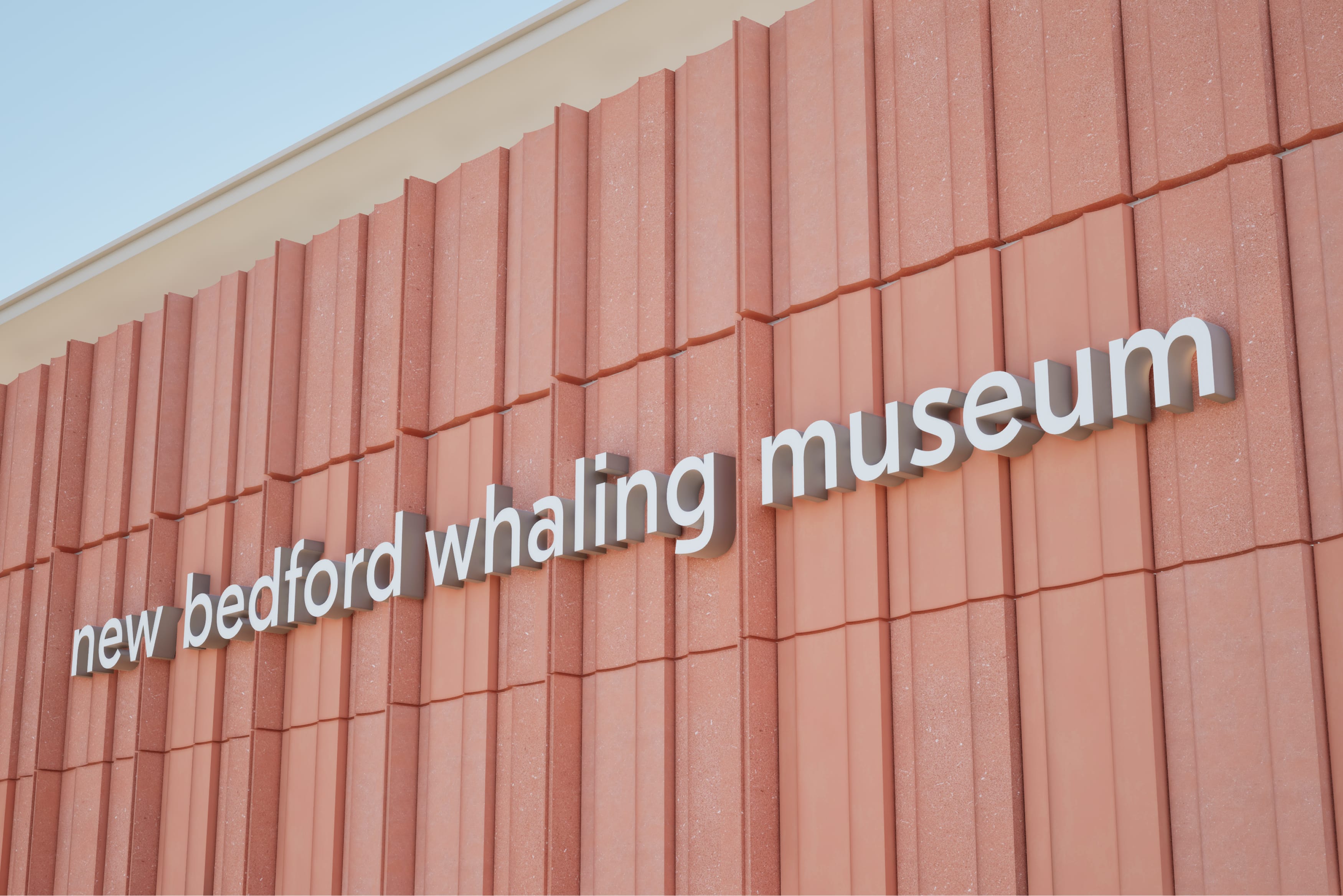 Dimensional lowercase lettering spelling "new bedford whaling museum" on a corten steel wall panel facade, exterior building identification signage by RSM Design