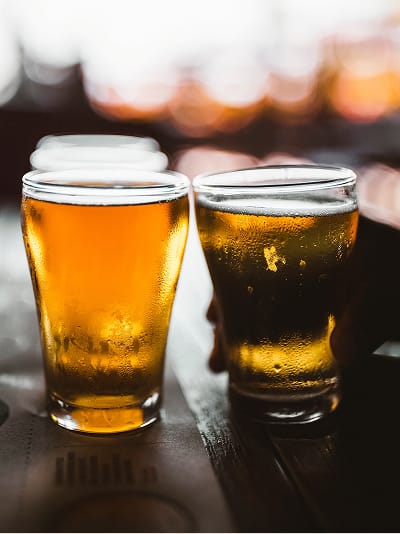 Two chilled beer glasses with condensation on dark wood bar with warm bokeh lighting, brand identity lifestyle imagery at Avenue South by RSM Design.