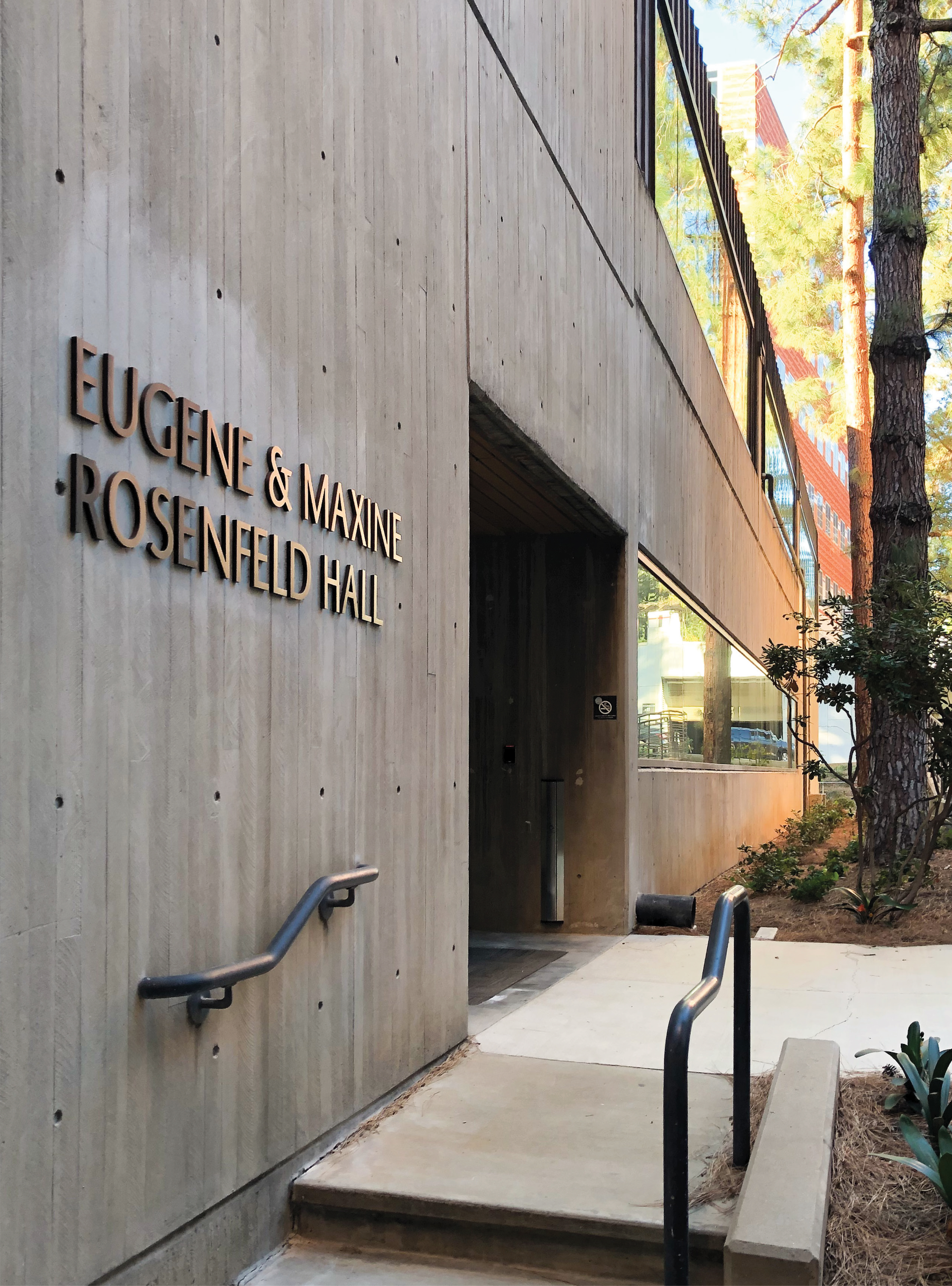 Architectural building identification signage for Eugene & Maxine Rosenfeld Hall on a university campus, demonstrating environmental graphic design, campus placemaking, and integrated wayfinding within the higher education built environment.