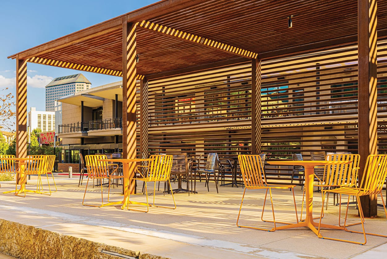 Shaded outdoor patio seating area with warm wood pergola structure at Toyota Music Factory mixed-use entertainment district in Irving, Texas — RSM Design placemaking and experiential design for mixed-use, food and beverage, and streetscape destinations where human-centered environments connect people to place.