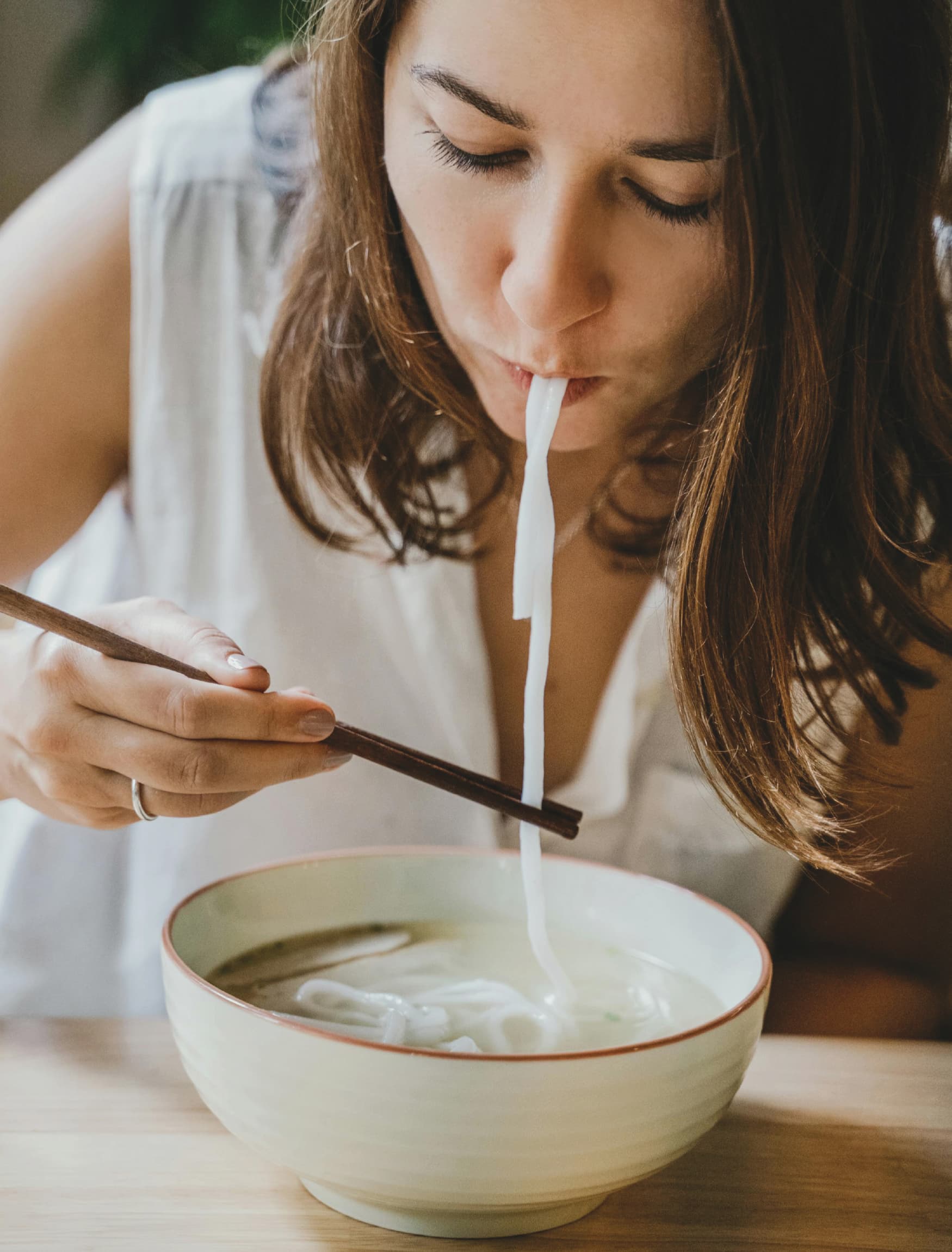 Image of a woman eating soup or pho at a restaurant. 