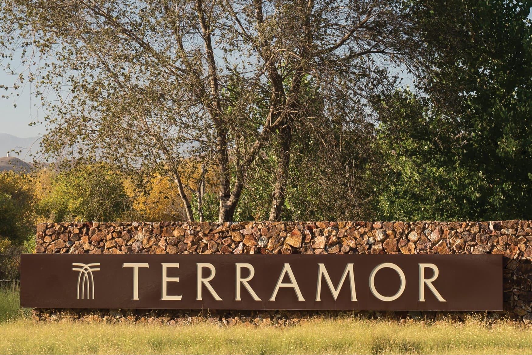 "Terramor" monument sign with logo mark set on a stone base beneath trees - environmental graphic design by RSM Design