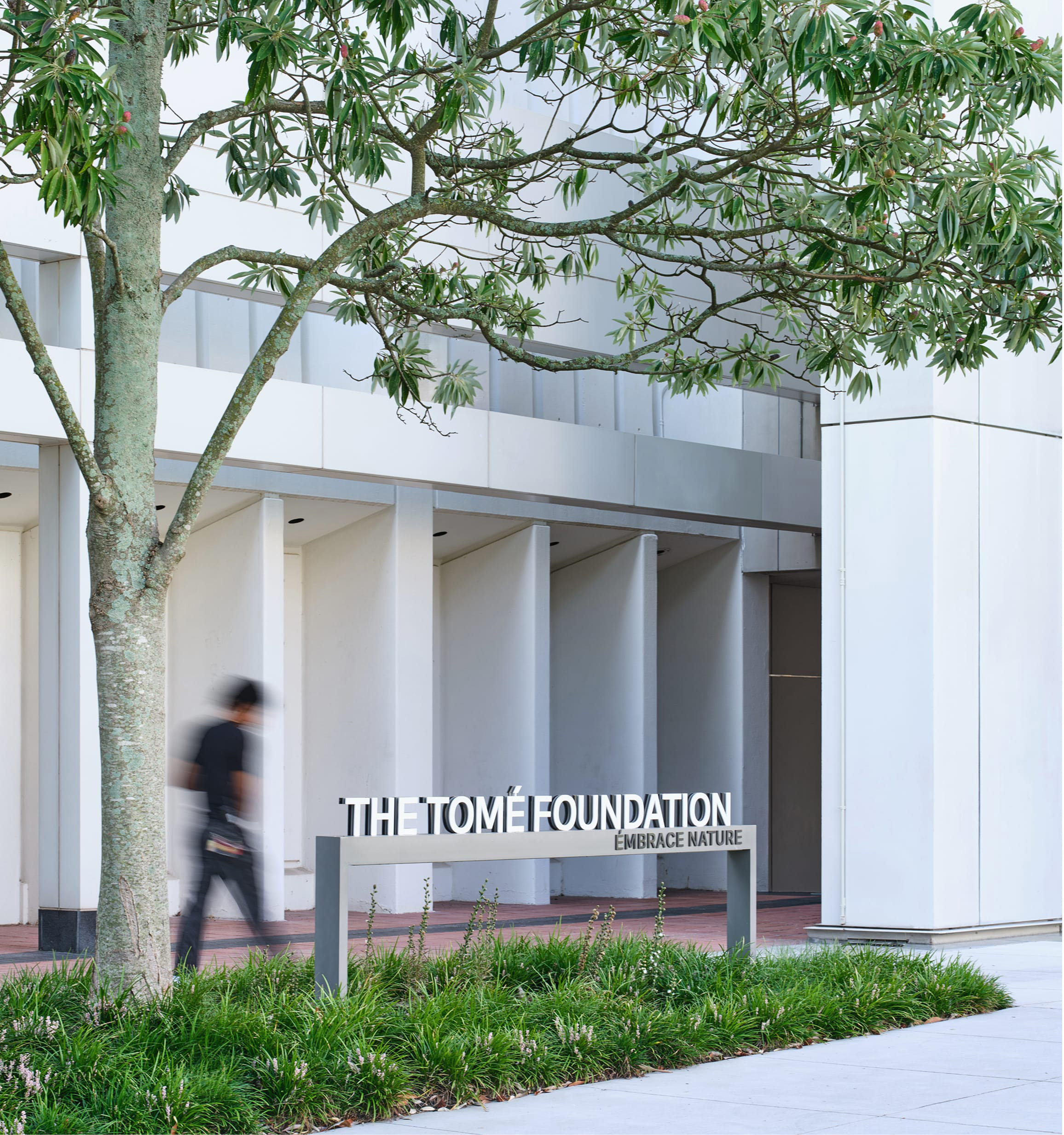 Dimensional donor recognition sign reading "THE TOMÉ FOUNDATION, EMBRACE NATURE" set on a landscaped bed beneath a tree, in front of a colonnaded entrance at the Woodruff Arts Center – donor recognition and environmental graphic design by RSM Design.