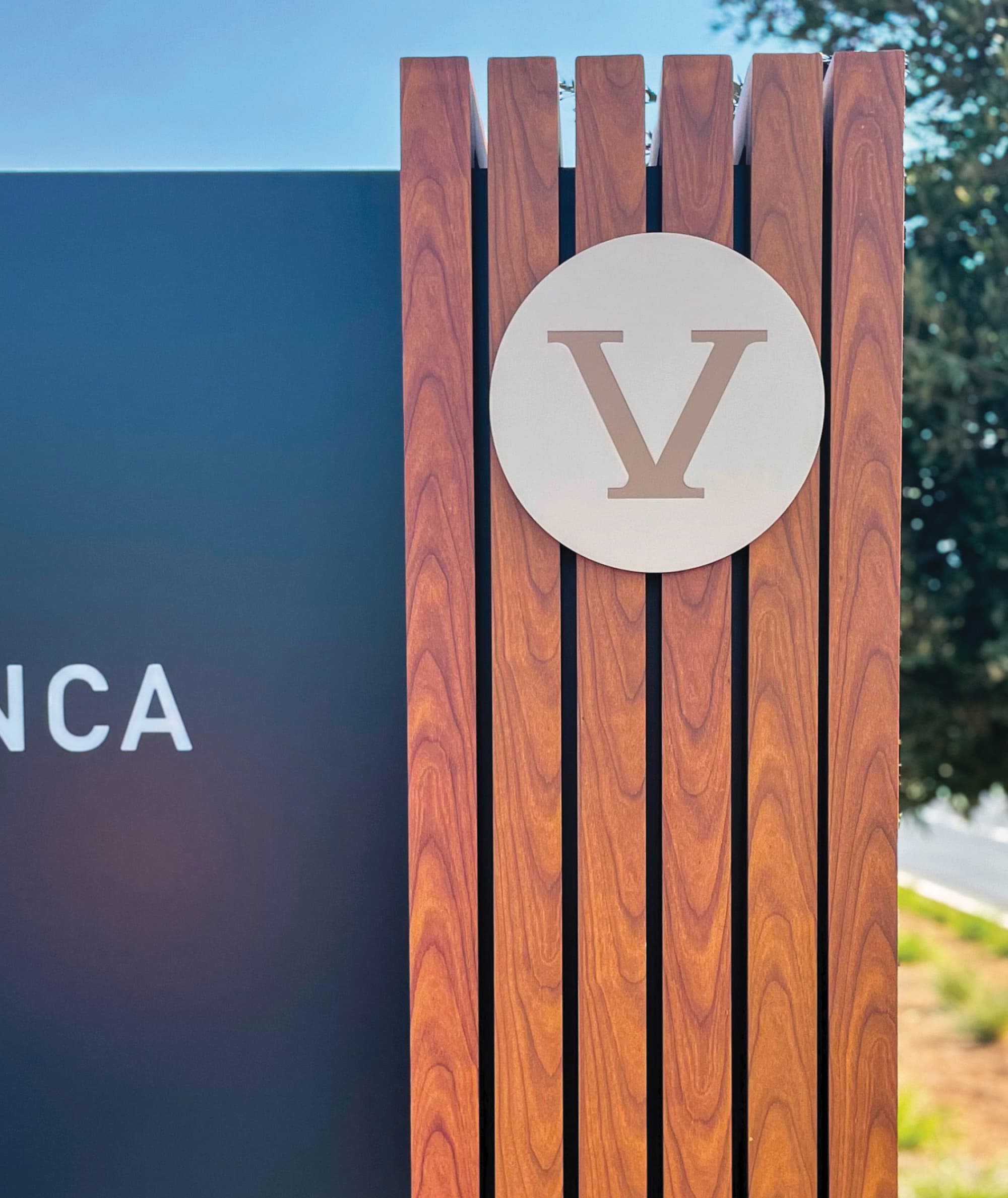Detail of a Fivepoint branded monument sign featuring vertical wood slats and a circular Fivepoint logo emblem with dimensional lettering. This custom exterior signage solution integrates architecture, materials, and brand strategy to create a cohesive sense of place within a healthcare and mixed-use campus environment.