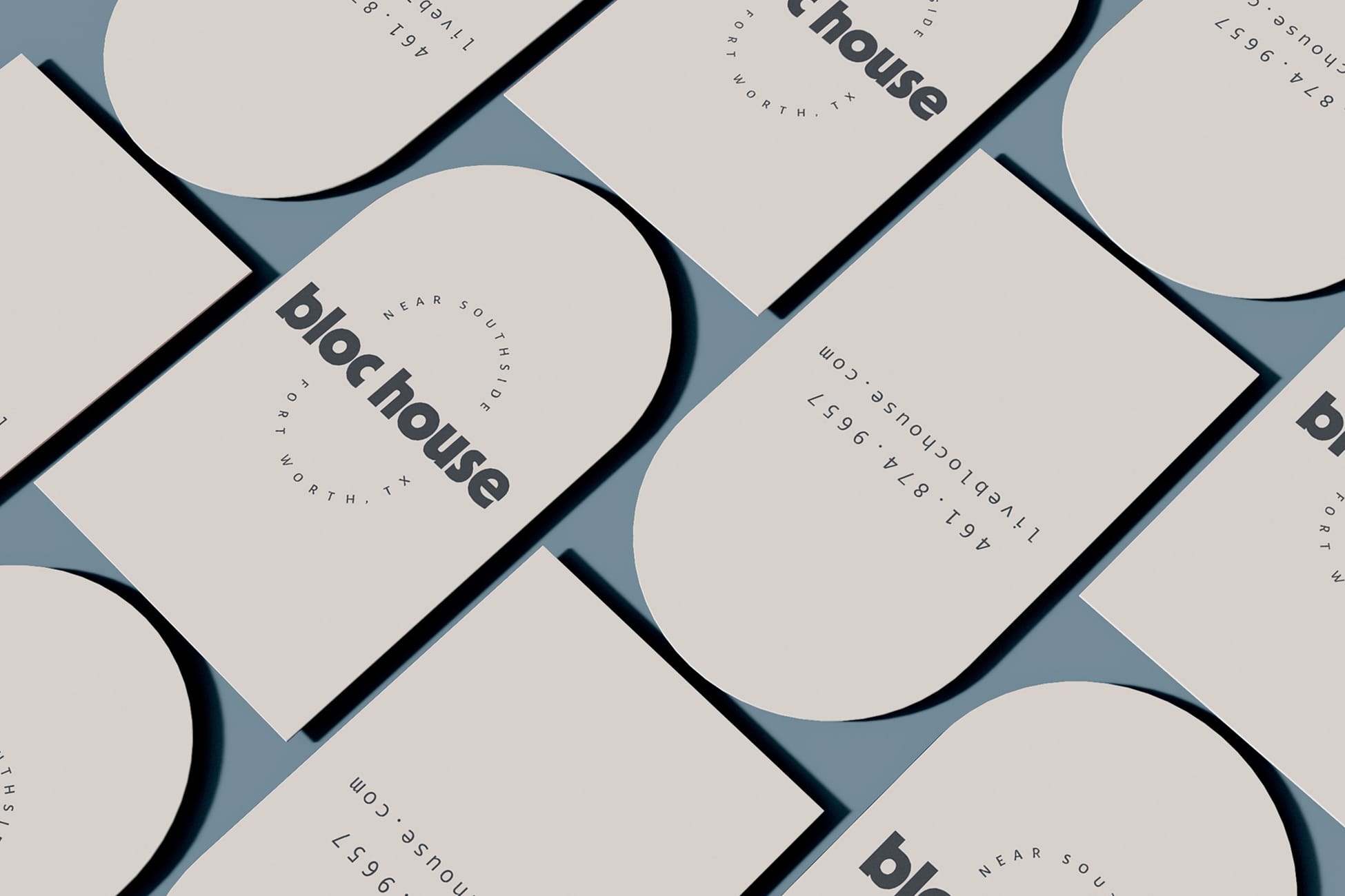 Bloc House business card mockup showing multiple cards arranged on a slate blue surface. The cards feature a cream background with a bold arch graphic, the "bloc house" wordmark, and "Near Southside, Fort Worth, TX" set in circular type. 