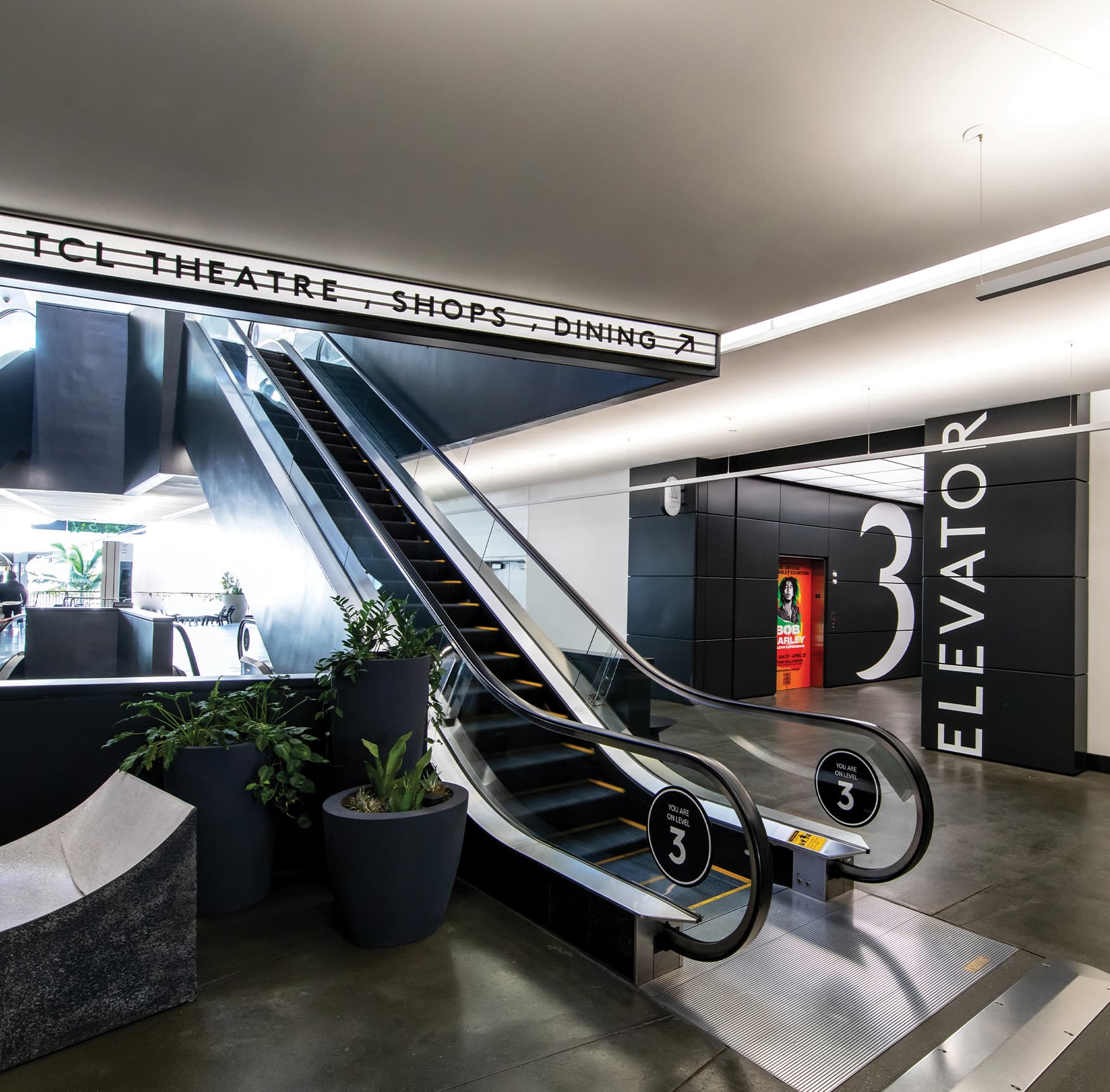 Black and white overhead directional above escalator entry with elevator vestibule graphics to the right by RSM Design for Ovation Hollywood in Los Angeles, California