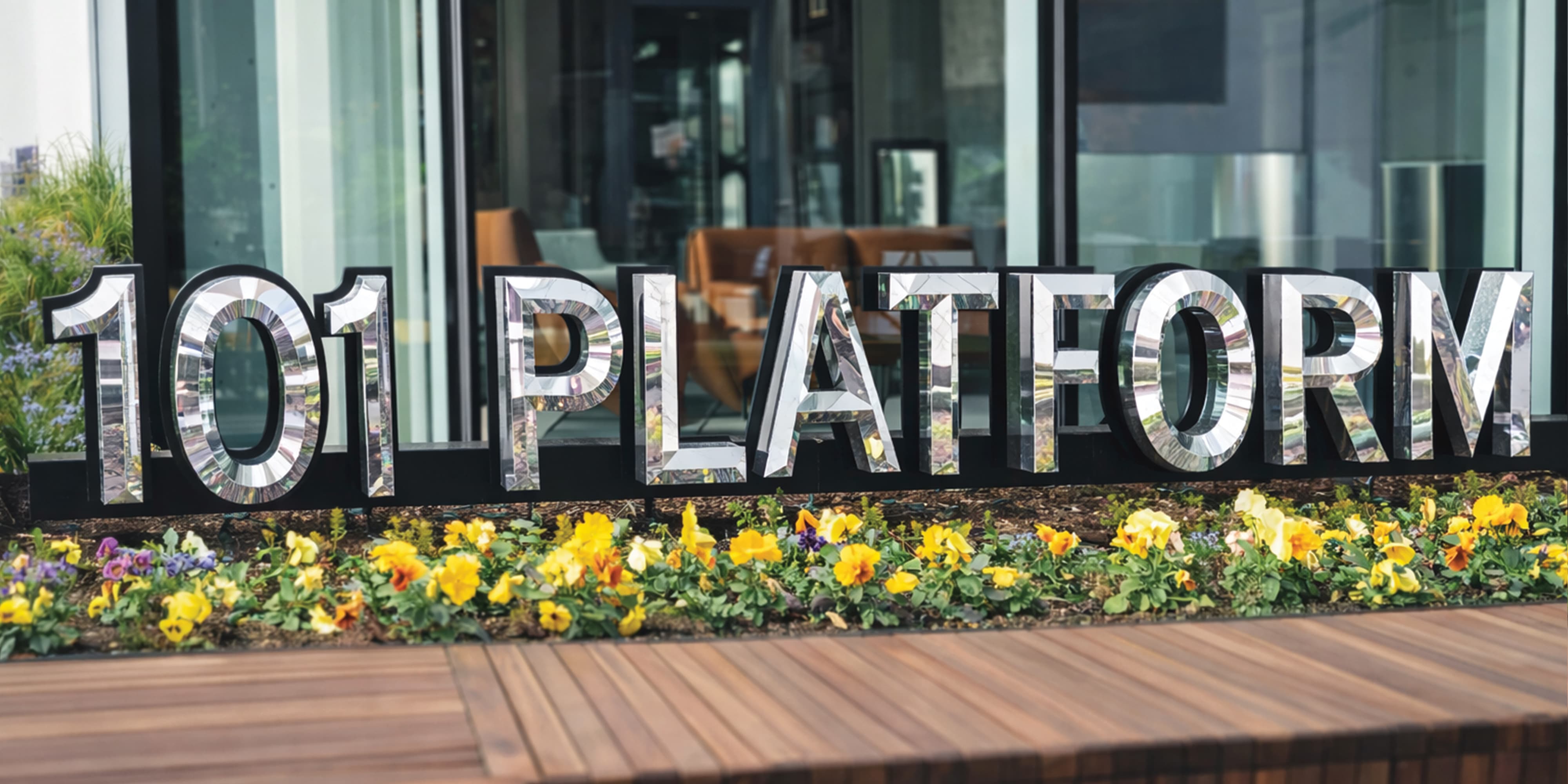 Large-scale dimensional mirrored "101 Platform" letters nestled in a flowering garden bed at a mixed-use development entrance, showcasing placemaking, experiential graphics, and branded environment design by RSM Design.