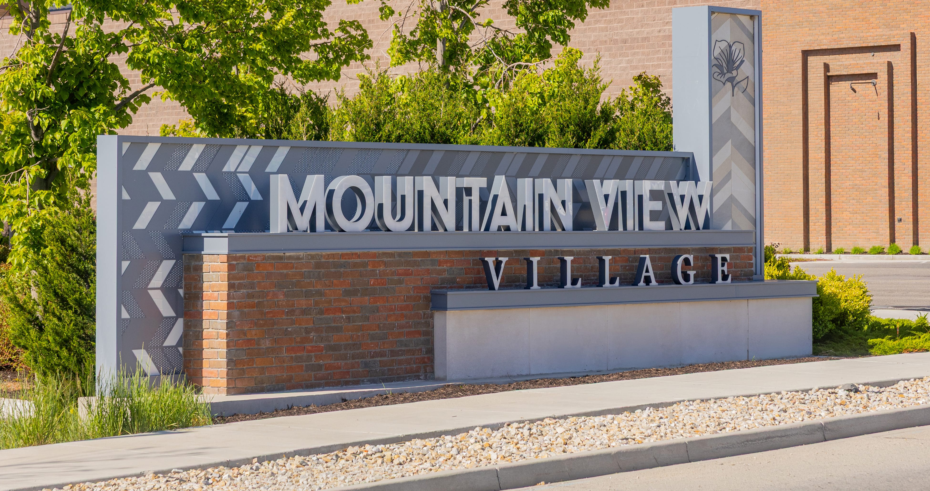 Monument sign with dimensional "Mountain View Village" lettering on a brick and metal chevron-patterned base, with a sego lily emblem panel, at the Riverton, Utah center — environmental graphic design and monument signage by RSM Design.