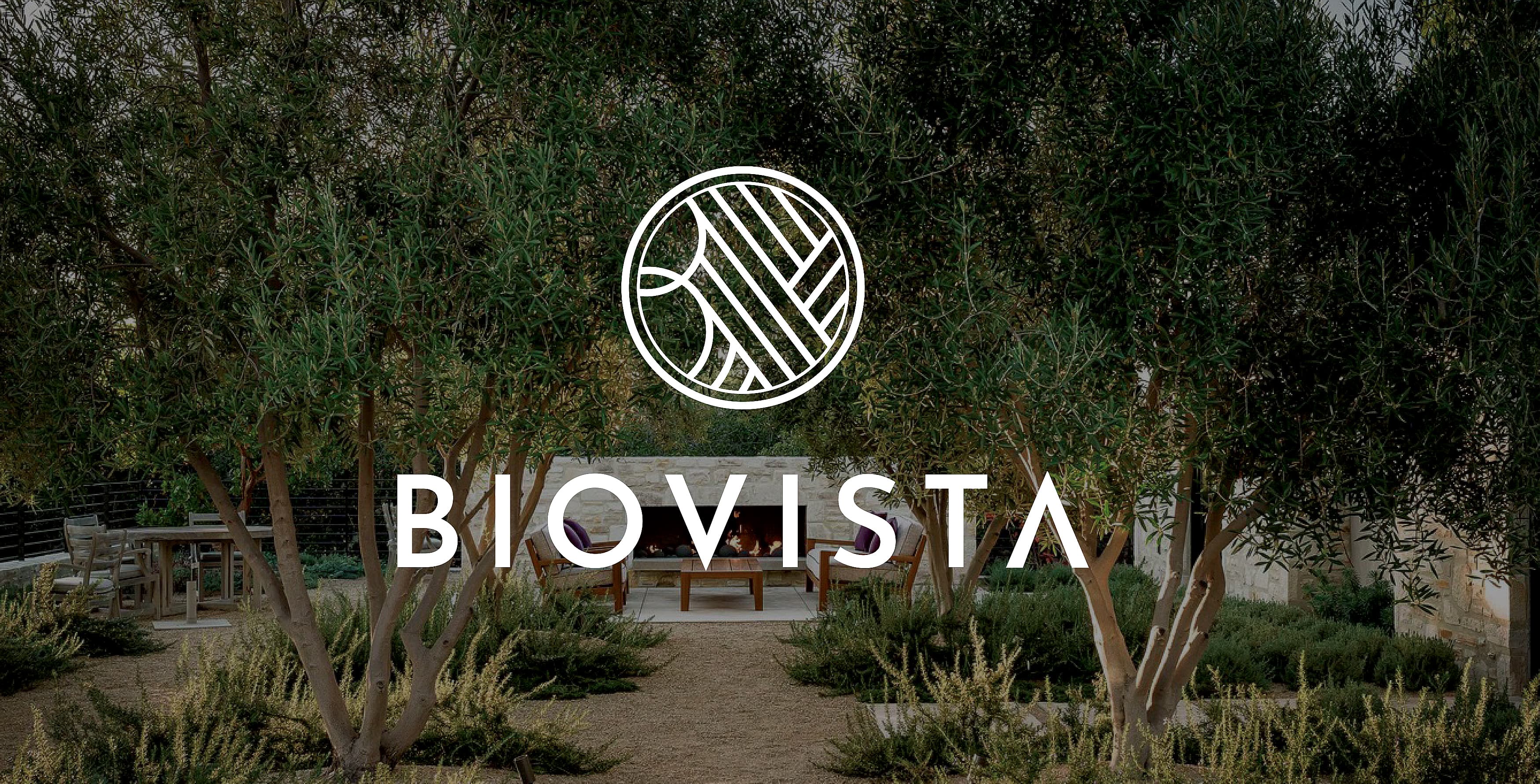 Primary BioVista wordmark and icon logo in white overlayed on top of an image of an outdoor courtyard with sitting areas and greenery and landscape.