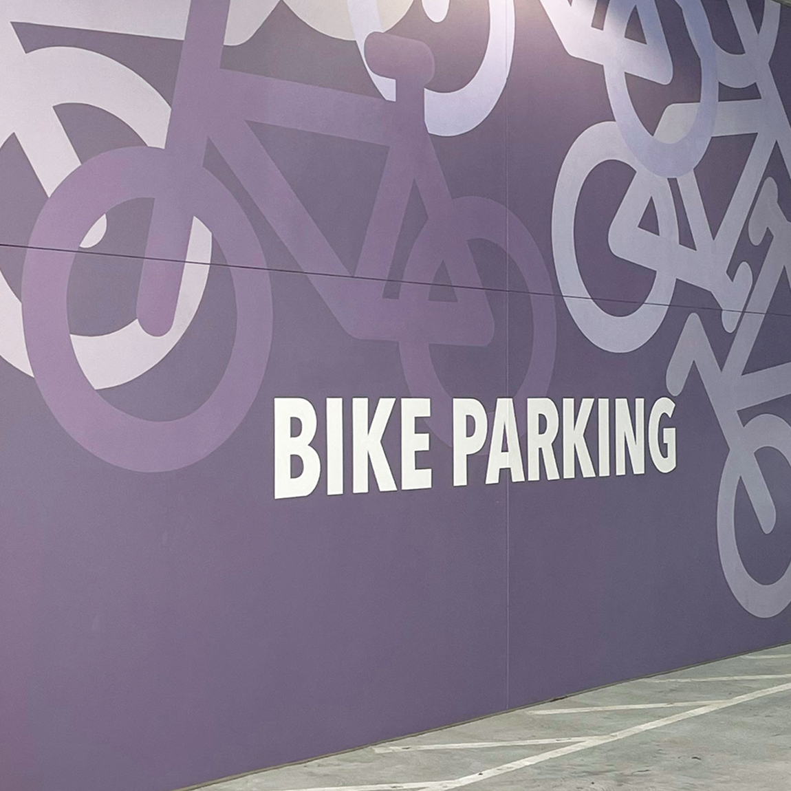 Purple bike parking wayfinding wall mural with oversized bicycle graphics in parking structure at 825-835 San Carlos, interior environmental graphic design by RSM Design