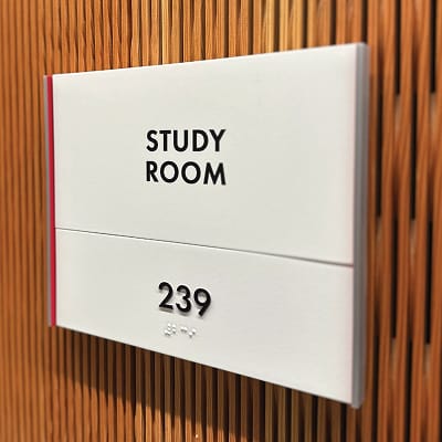 RSM Design Chapman University Rinker Campus Center Irvine — ADA-compliant study room identification sign with Braille, room number 239, Chapman red side trim, mounted on warm wood slat wall