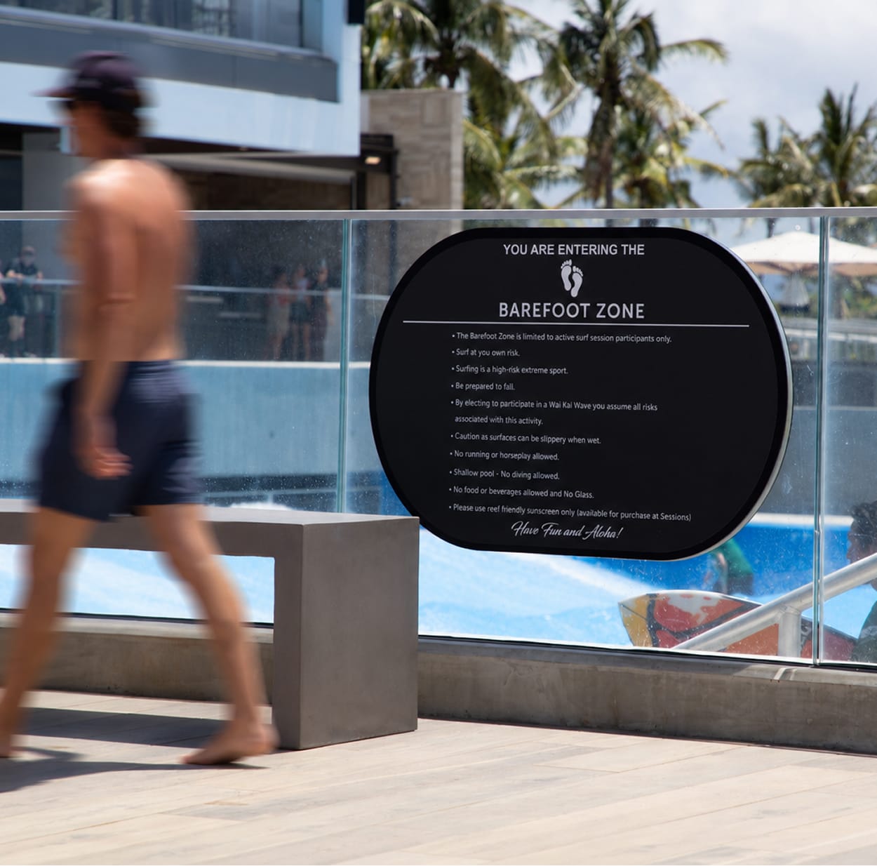 "Barefoot Zone" oval regulatory sign mounted on glass railing overlooking wave pool at Wai Kai, Ewa Beach, Oahu, wayfinding by RSM Design.