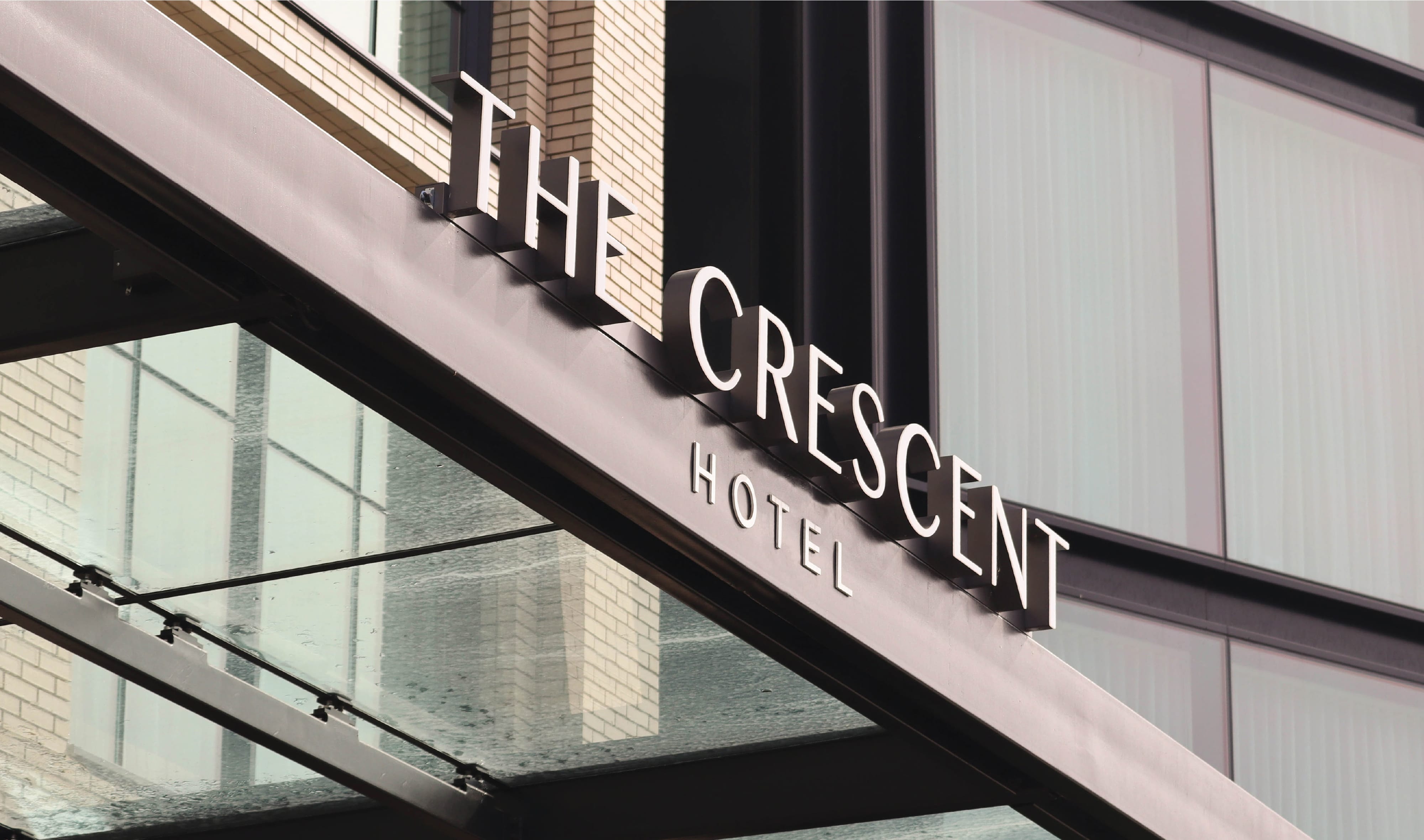 The Crescent Hotel illuminated exterior entrance canopy signage with bold dimensional lettering against a modern glass and brick facade, showcasing the brand identity of an upscale boutique hotel
