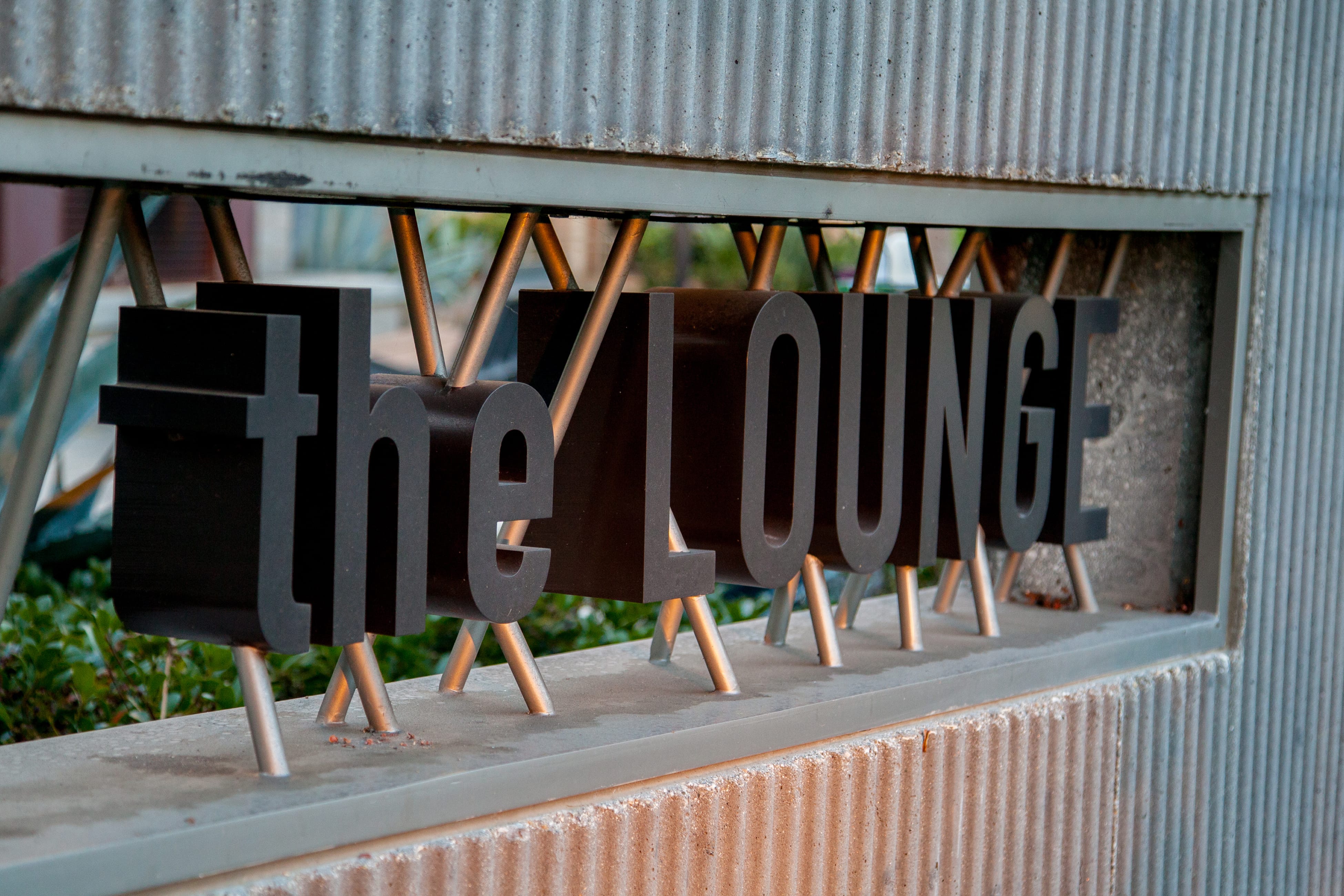 Dimensional sign reading "the LOUNGE," designed by RSM Design, with letters suspended on metal struts beneath a corrugated metal canopy in Playa Vista.