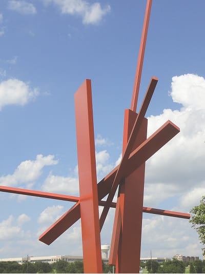 Red steel abstract sculpture of intersecting beams against a blue sky at Hall Park