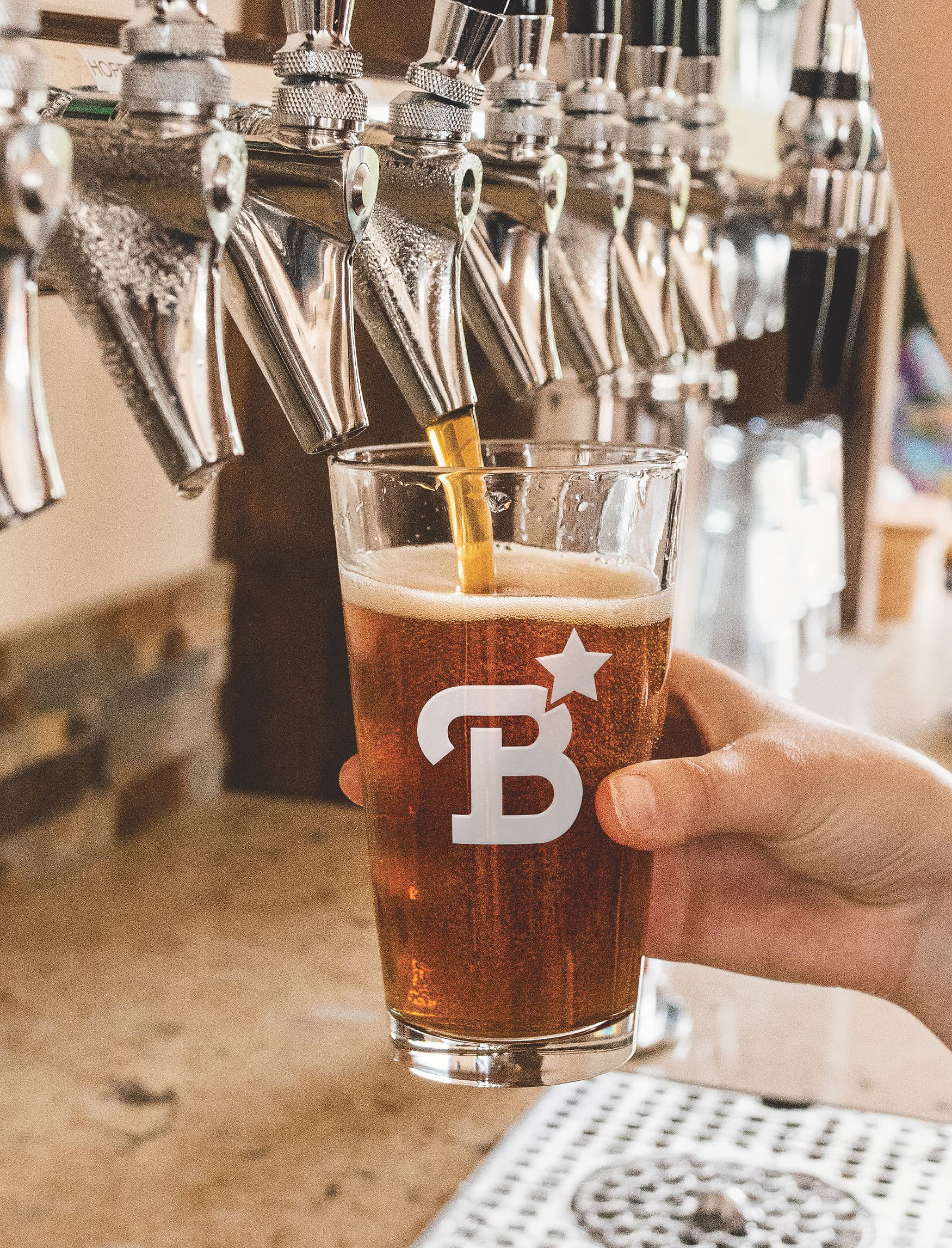 Craft beer being poured into a branded The Bend HTX pint glass at a bar tap, highlighting brand identity design, placemaking, and experiential branding for a mixed-use retail, dining, and entertainment destination.