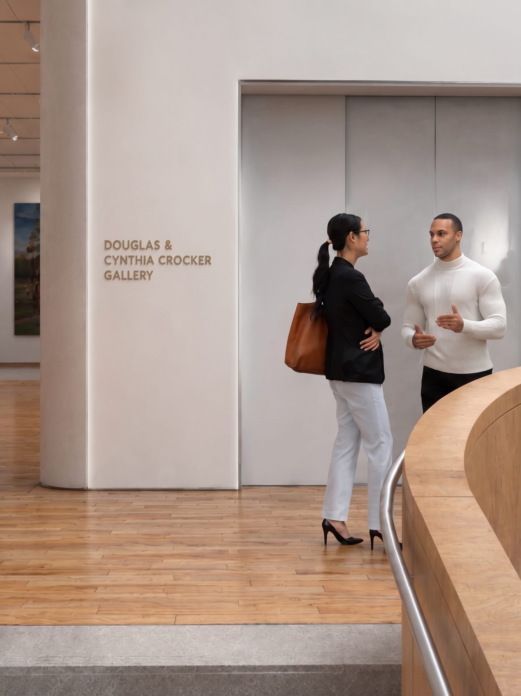 Bronze dimensional lettering reading "Douglas & Cynthia Crocker Gallery" on a curved gallery wall near a wood-clad staircase, donor recognition signage by RSM Design
