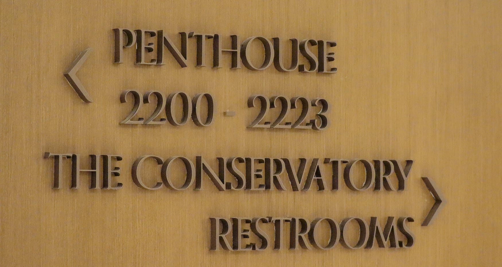 Wood directional sign with custom Art Deco typography guiding to the Penthouse, Conservatory, and Restrooms at Maple Terrace - environmental graphic design by RSM Design