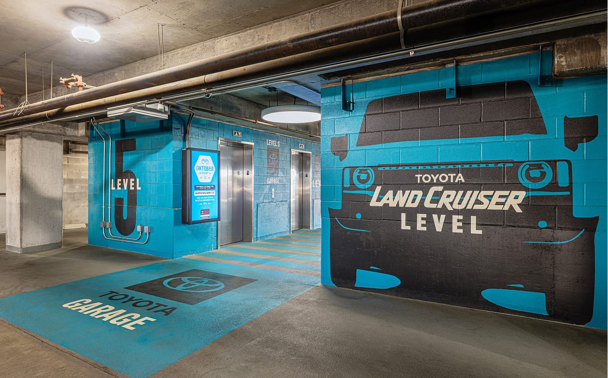 Branded parking garage elevator lobby on Level 5 featuring Toyota Land Cruiser large-scale wall murals, floor graphics, digital display signage, and level identification graphics at Toyota Music Factory in Irving, Texas — RSM Design wayfinding and signage design, experiential graphics, digital integration, branded environments, and master sign programs for parking garage and mixed-use destinations.