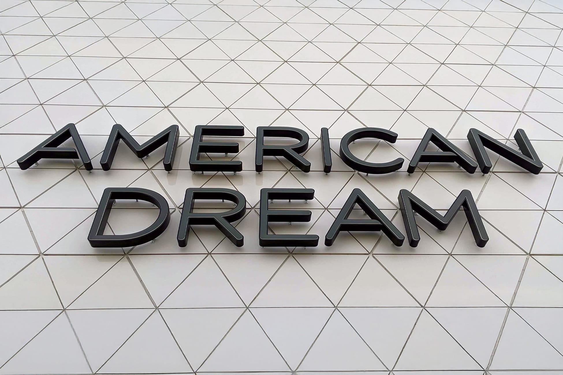 Close-up of large-scale dimensional channel letter wall signage reading 'American Dream' in matte black mounted on a geometric white tile facade at American Dream mall in East Rutherford, New Jersey — showcasing RSM Design's architectural graphics, environmental graphic design, and branded environments for a large-scale mixed-use retail and entertainment destination.