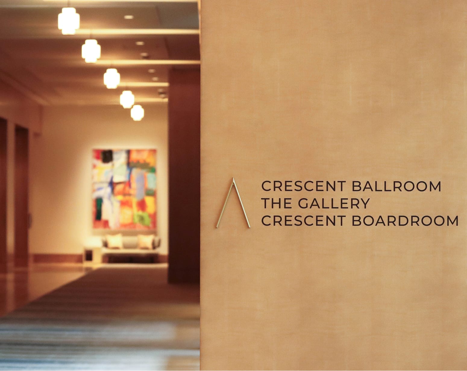 The Crescent Hotel event venue signage directing guests to the Crescent Ballroom, The Gallery, and Crescent Boardroom, with a warmly lit hallway featuring colorful abstract artwork and pendant lighting in the background