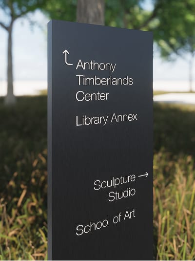 Close-up rendering of University of Arkansas Windgate Arts and Design District charcoal wayfinding bollard with white directional text guiding visitors to Anthony Timberlands Center, Library Annex, Sculpture Studio, and School of Art