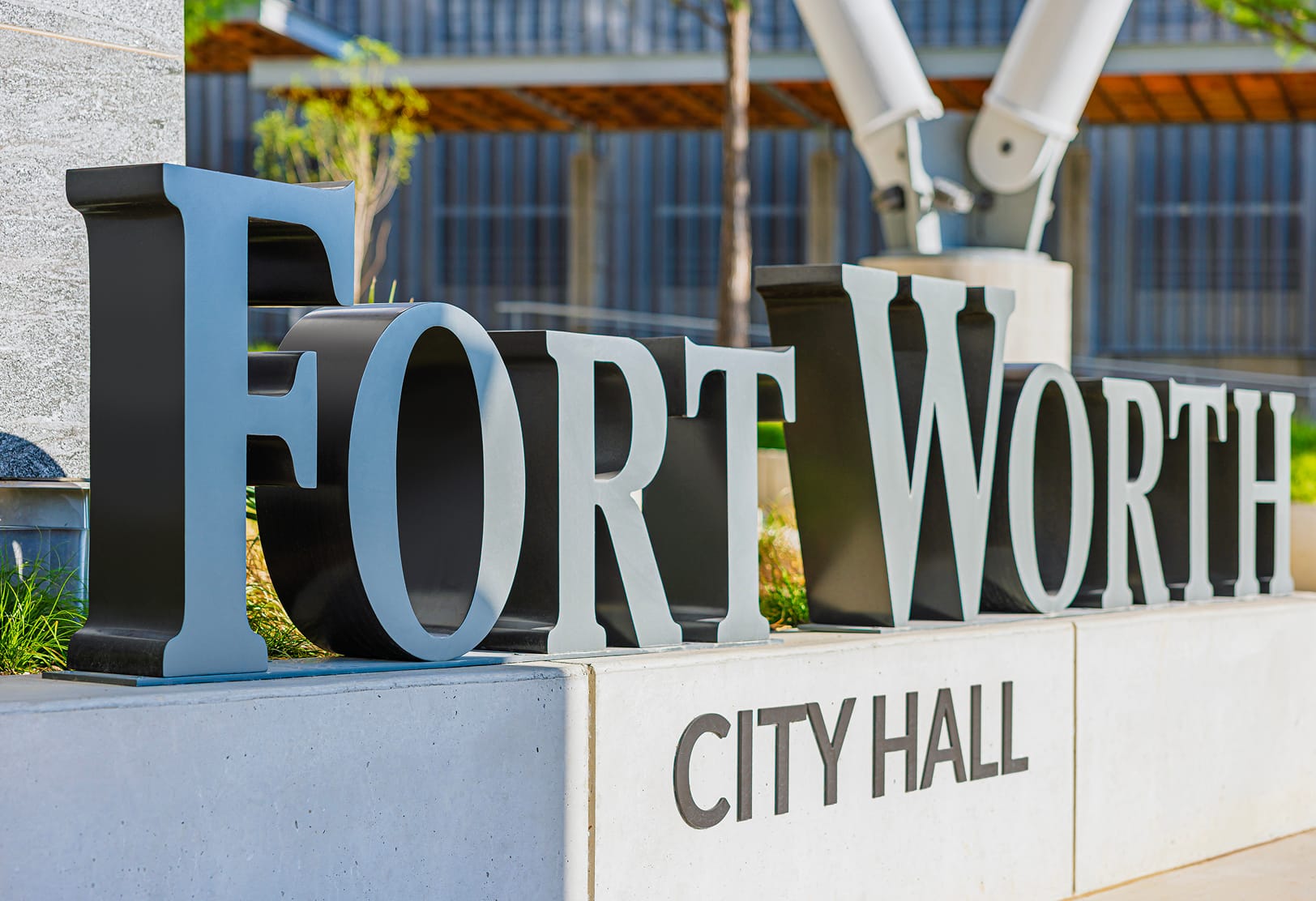 Close-up of Fort Worth City Hall dimensional letter monument sign featuring large black and light blue serif letters on concrete base with structural column and wood canopy in background
