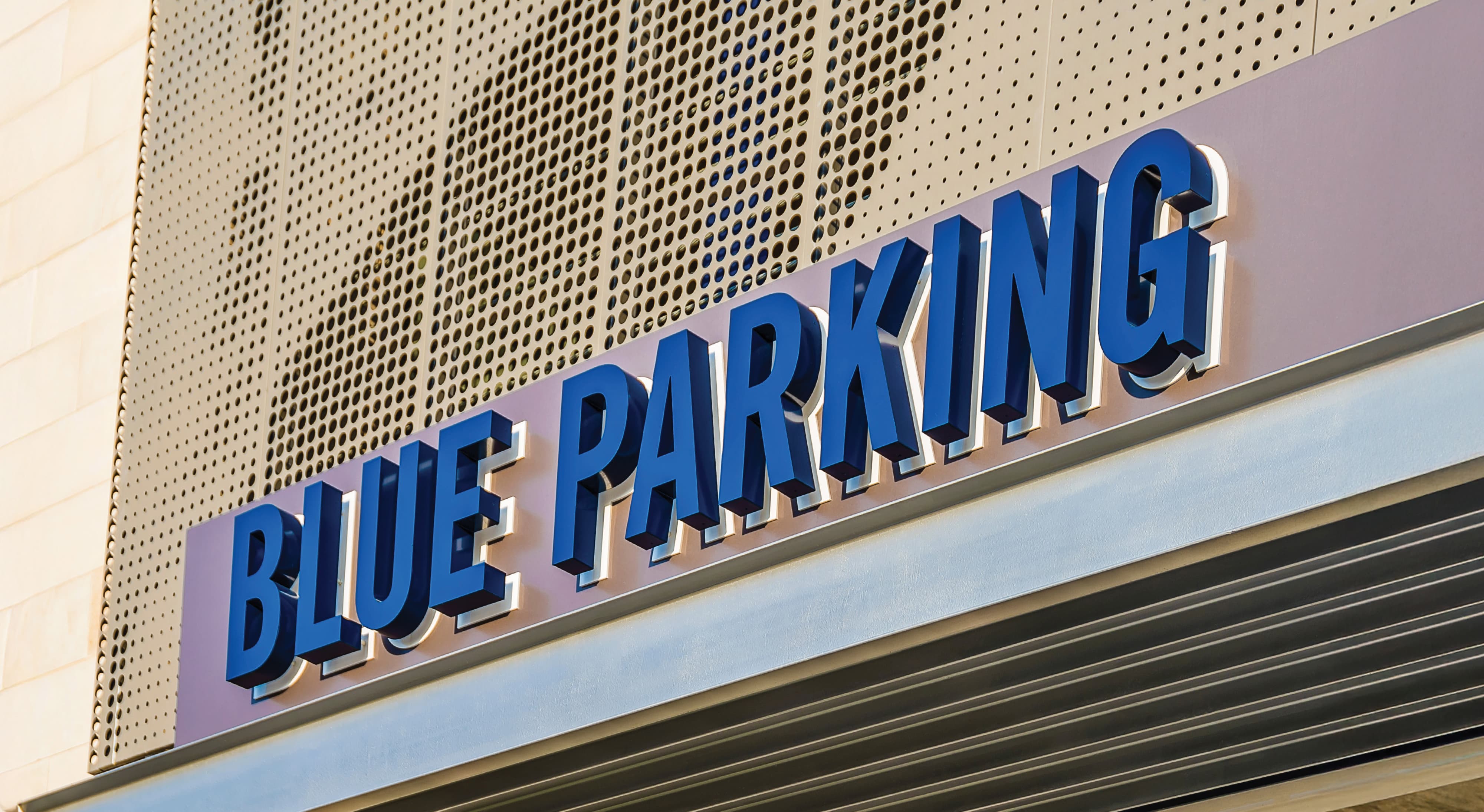 Close-up of dimensional letter 'Blue Parking' identification signage mounted on a perforated metal facade at a mixed-use sports and entertainment destination — showcasing RSM Design's architectural graphics and wayfinding signage design for a parking garage environment.
