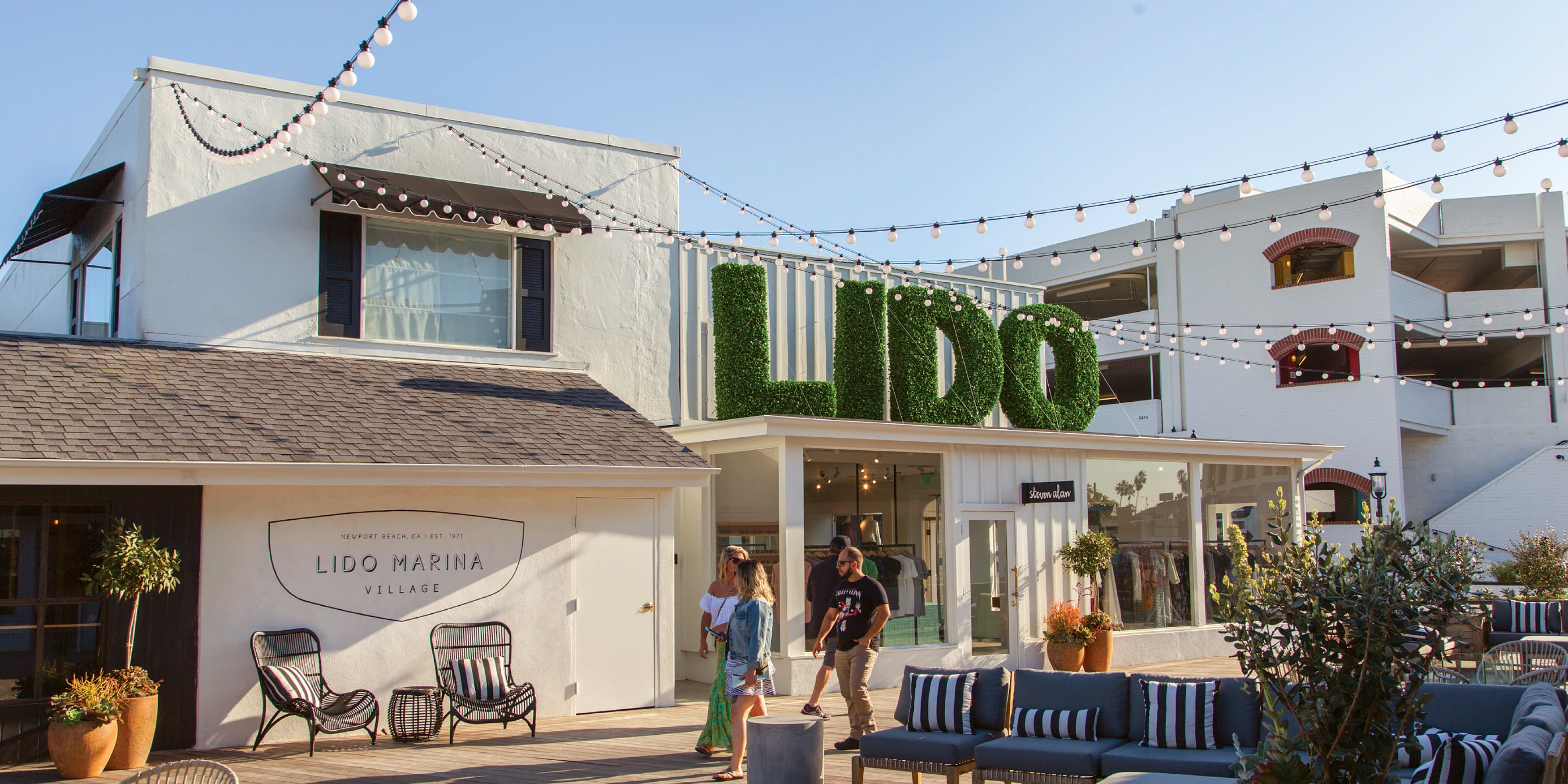 An open plaza at Lido Marina Village in Newport Beach with seats and large LIDO letters wrapped with faux greenery