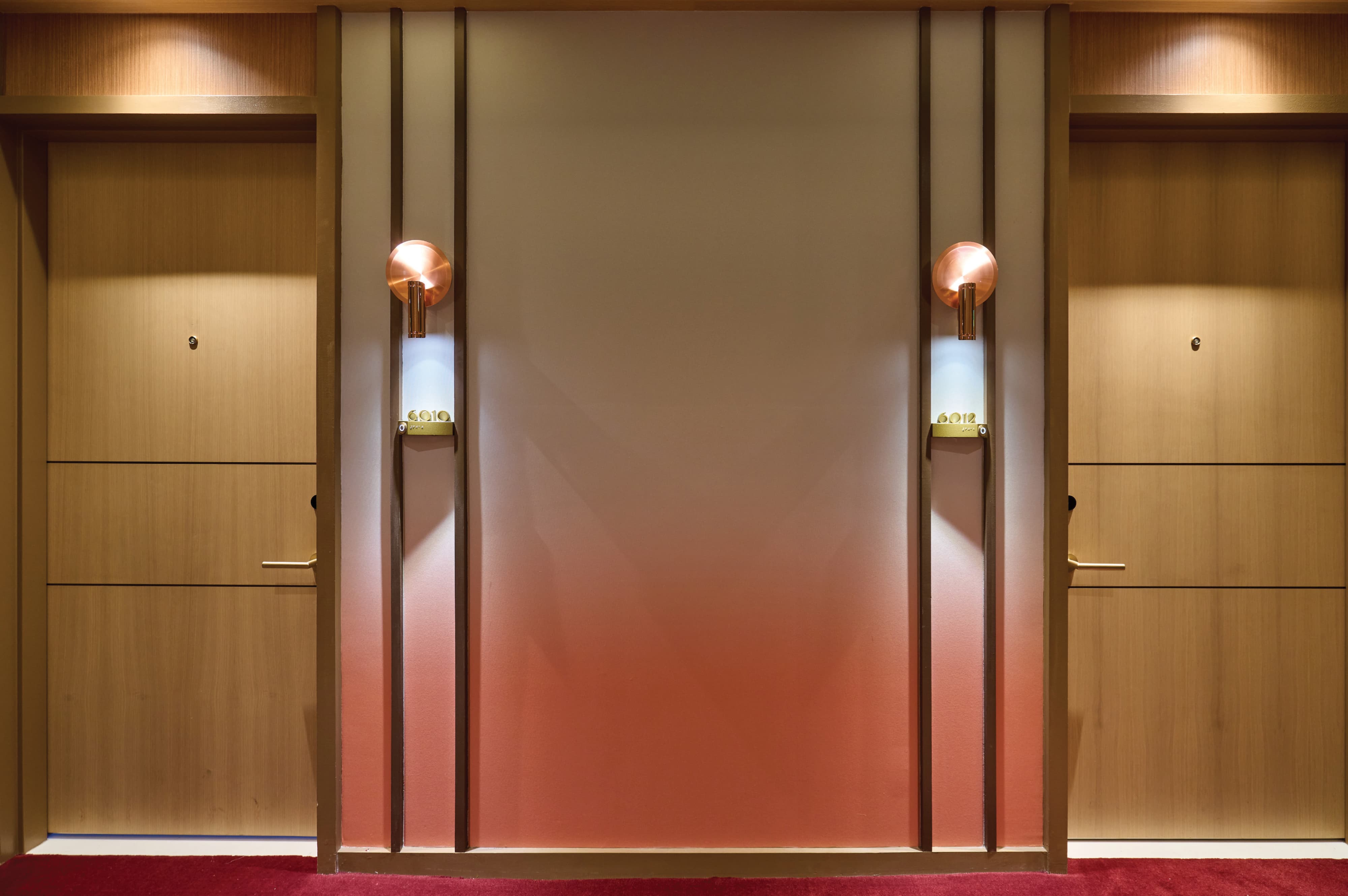 Symmetrical hotel guest room corridor with brushed brass ADA-compliant room identification signs, copper wall sconces, warm wood veneer doors, and gradient ombre feature wall at Pier Sixty-Six luxury waterfront resort in Fort Lauderdale, Florida — RSM Design wayfinding and signage design, master sign programs, specialty graphics, and branded environments for hospitality and waterfront destinations.