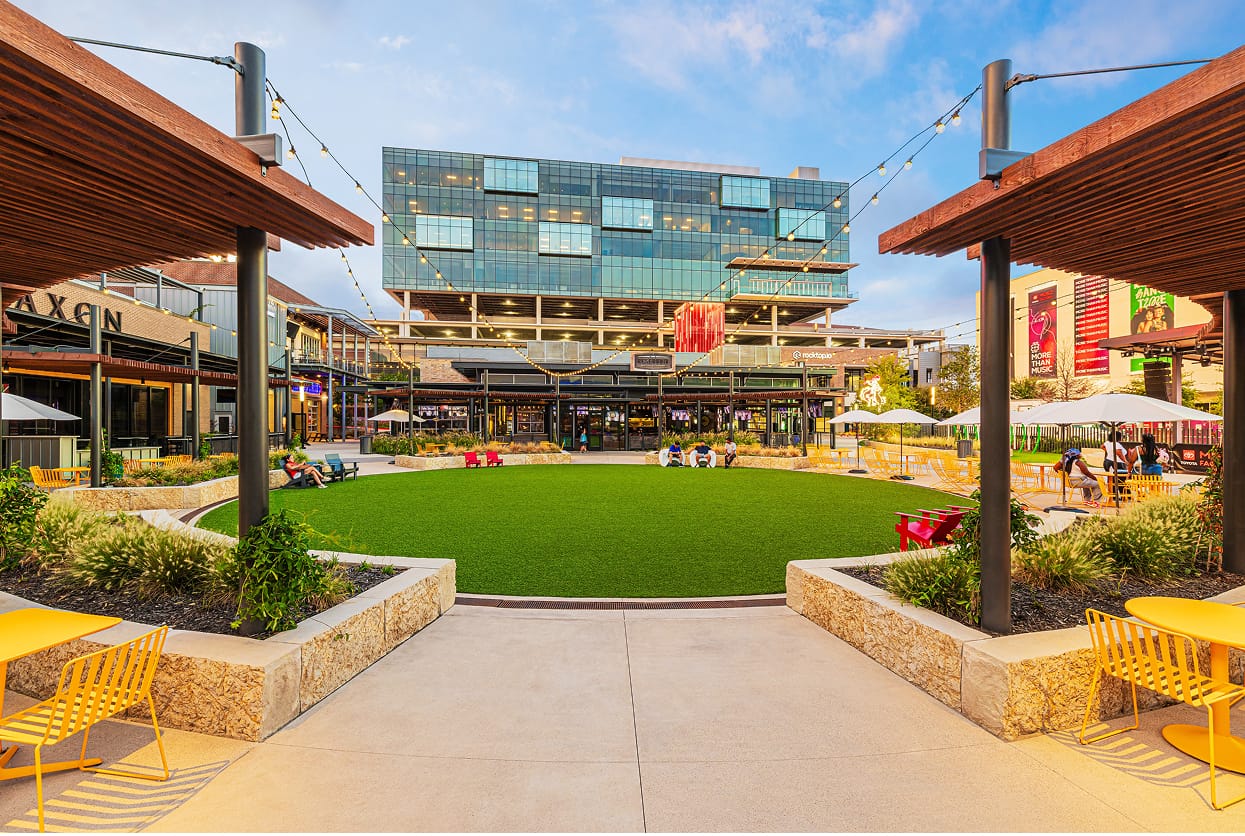 Activated outdoor plaza and public lawn at Toyota Music Factory mixed-use entertainment district in Irving, Texas, featuring tenant identification signage, experiential graphics, and branded environmental design — RSM Design placemaking, wayfinding and signage design, and experiential graphic design for mixed-use, food and beverage, retail, and streetscape destinations.