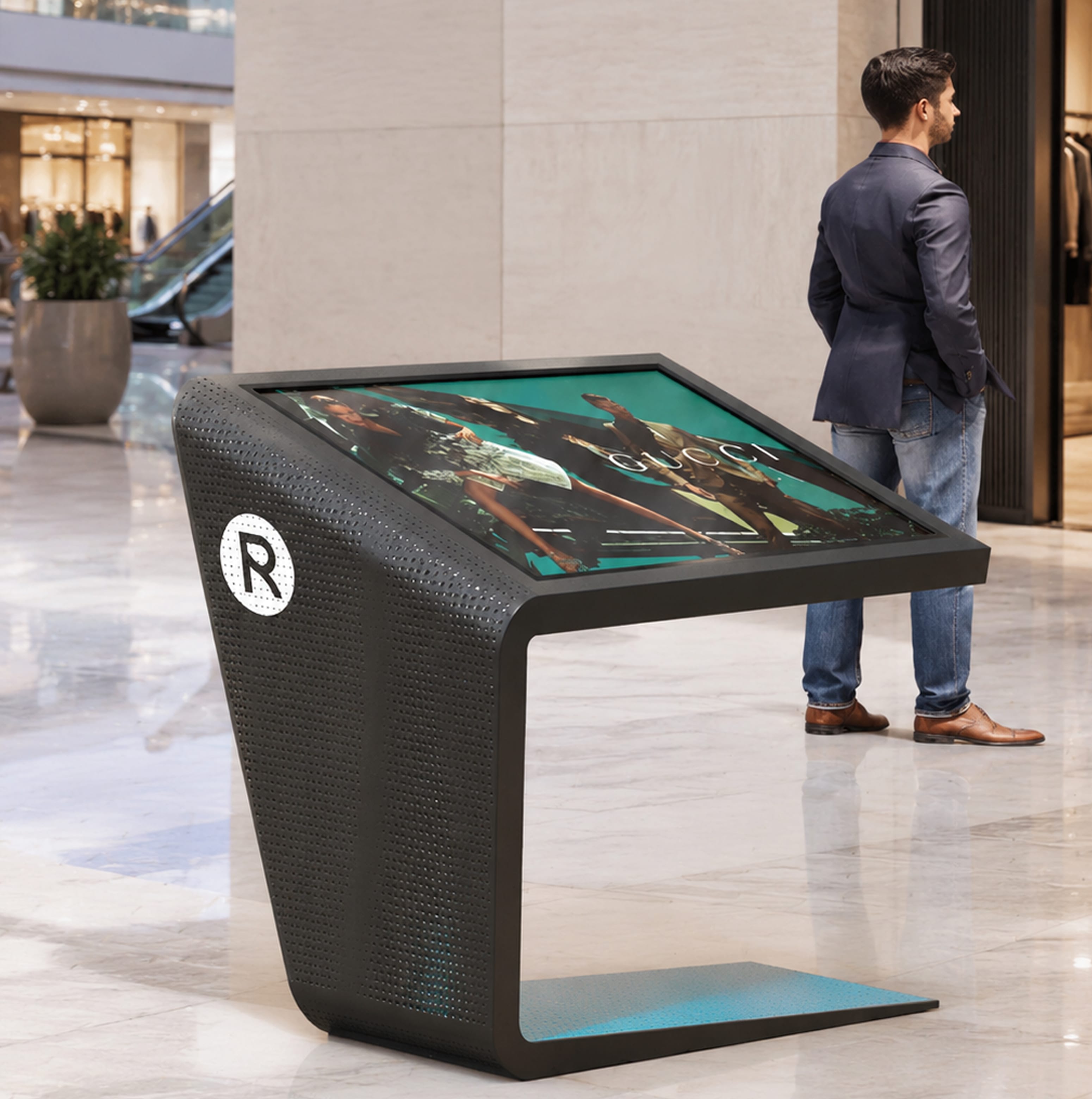Rendering of a black digital directory kiosk with "R" logo and Gucci ad display, man standing nearby in a marble-floored retail concourse — wayfinding kiosk design by RSM Design