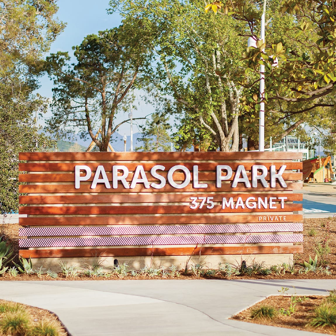 Parasol Park neighborhood entrance monument sign with white dimensional letters and red diagonal stripe accents mounted on a horizontal wood slat wall at 375 Magnet Private in Irvine, California, designed by RSM Design