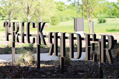 Trick Rider restaurant large-scale dimensional letter monument sign with dark metal cutout typography installed in native landscaping at Omni PGA Frisco