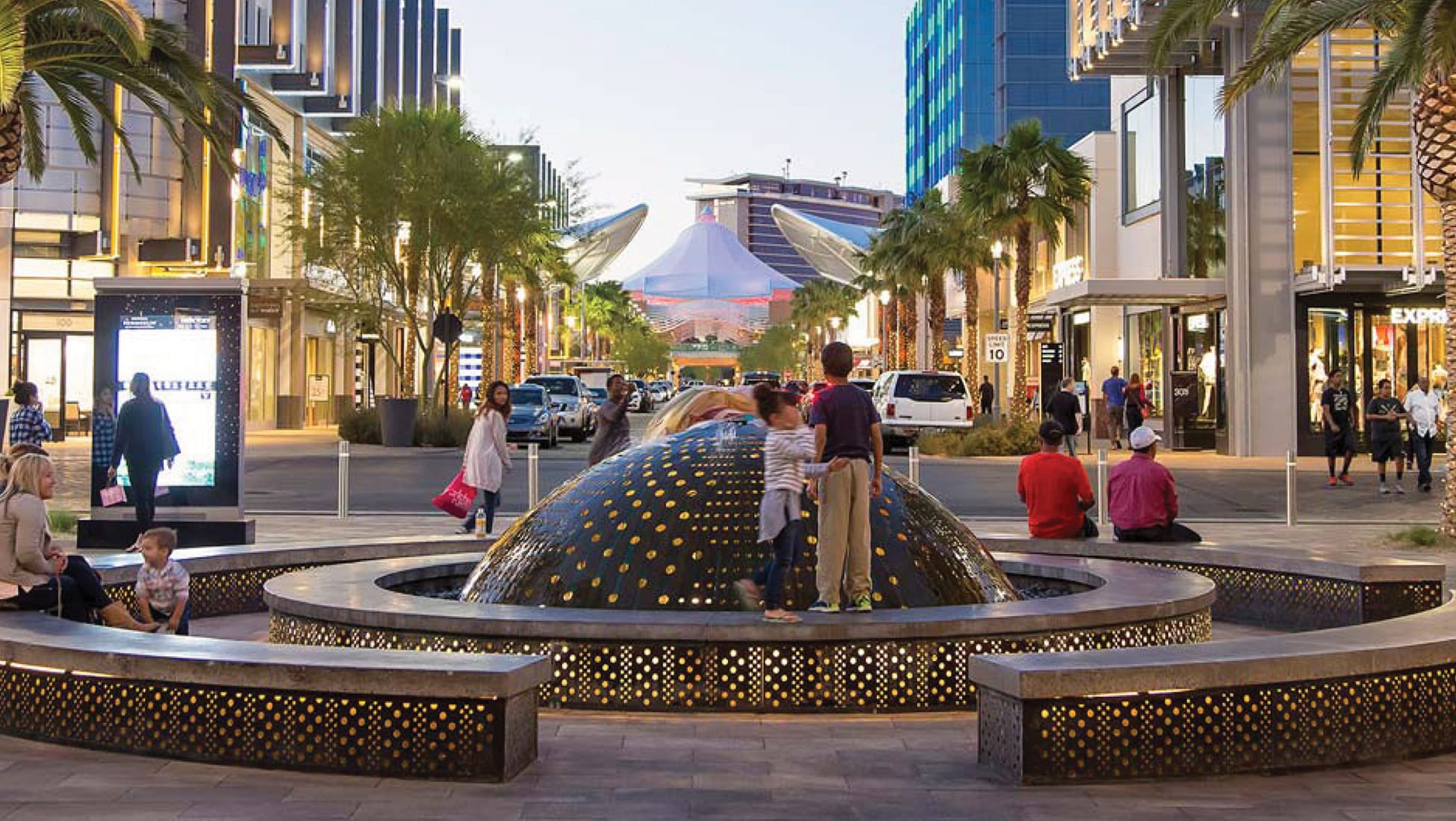 Summerlin Downtown Las Vegas streetscape featuring illuminated public art fountain, pedestrian plaza, retail storefronts, and active urban environment showcasing placemaking and experiential design by RSM Design.