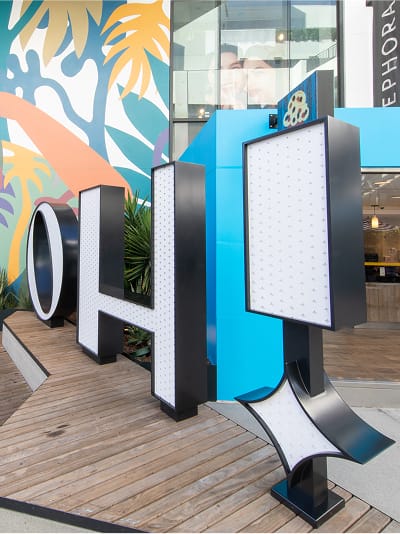 Ovation Hollywood "OH" large-scale illuminated letter sculpture installation with marquee bulb lighting and bold blue and black dimensional lettering in front of Sephora and tropical mural
