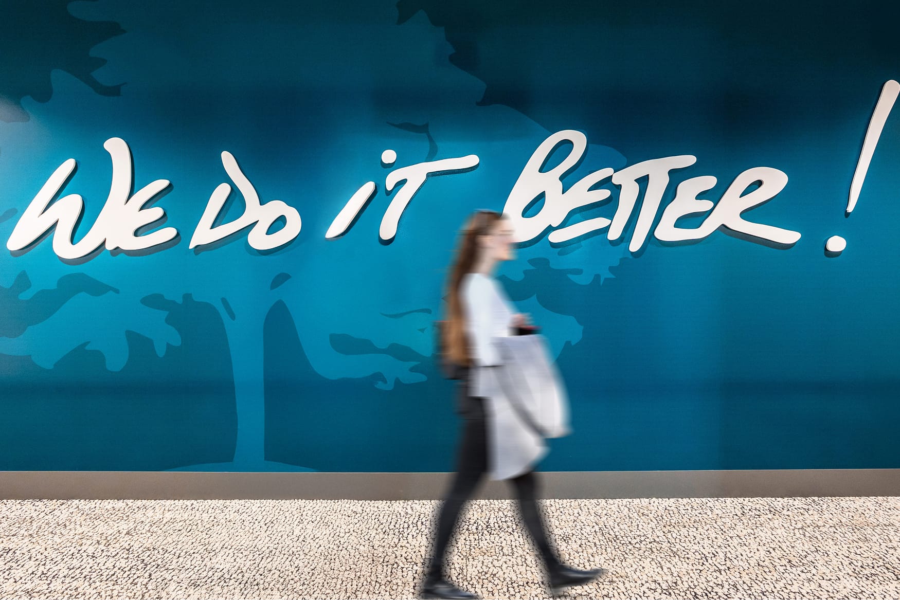 Environmental graphic design installation featuring large-scale branded messaging reading “We Do It Better!” within a workplace interior, showcasing experiential design, brand identity, and placemaking for corporate and media environments.