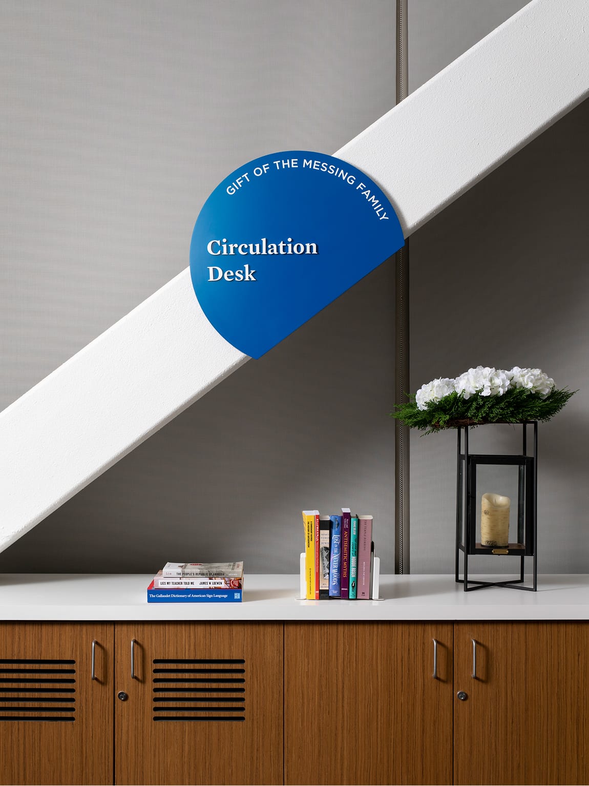 Circulation Desk donor sign mounted on angled architectural beam above library shelving at Brentwood School campus in Los Angeles - donor recognition and wayfinding design by RSM Design