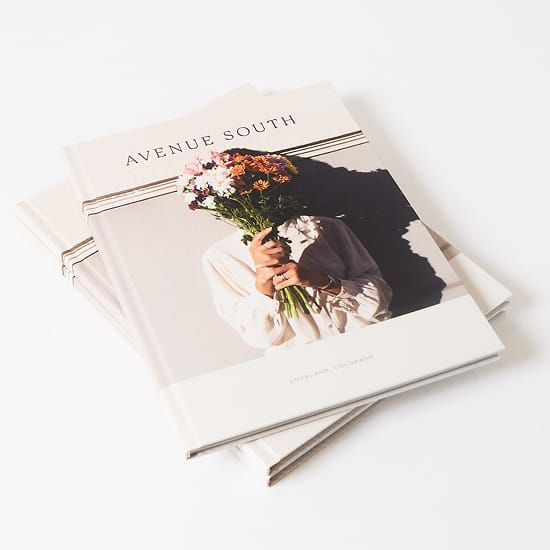 Stack of Avenue South brand books with cover photo of woman holding a bouquet, "Loveland, Colorado" printed below, brand identity book design by RSM Design.