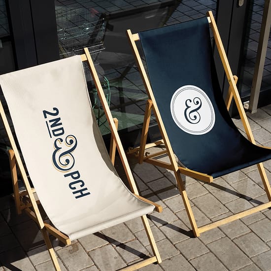 Branded canvas sling chairs displaying the 2nd & PCH logo and ampersand medallion mark in cream and navy — an example of RSM Design's print and digital collateral and branding and visual identity applied to experiential branded environments for a coastal waterfront retail and mixed-use destination in Long Beach, California.