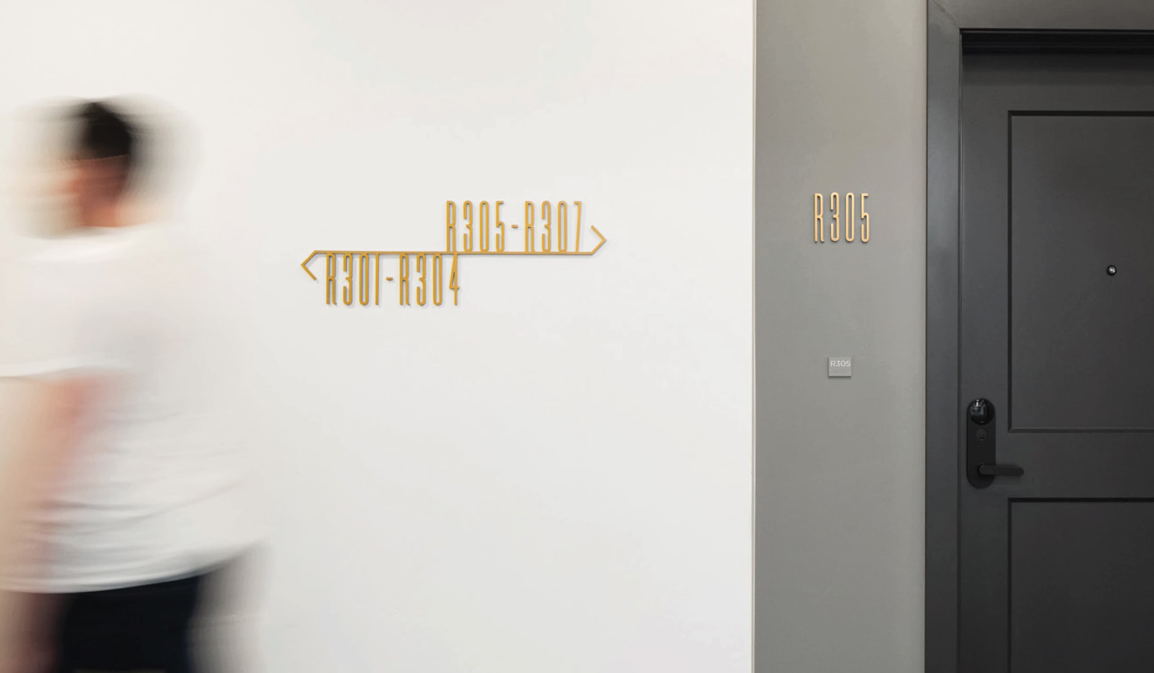 Interior corridor wayfinding signage at 801 Flats at Post District in Salt Lake City, featuring a gold dimensional unit-range directional sign on a white wall alongside a matching unit identification sign on a residential apartment door — showcasing RSM Design's wayfinding signage design and environmental graphic design for a mixed-use residential community.