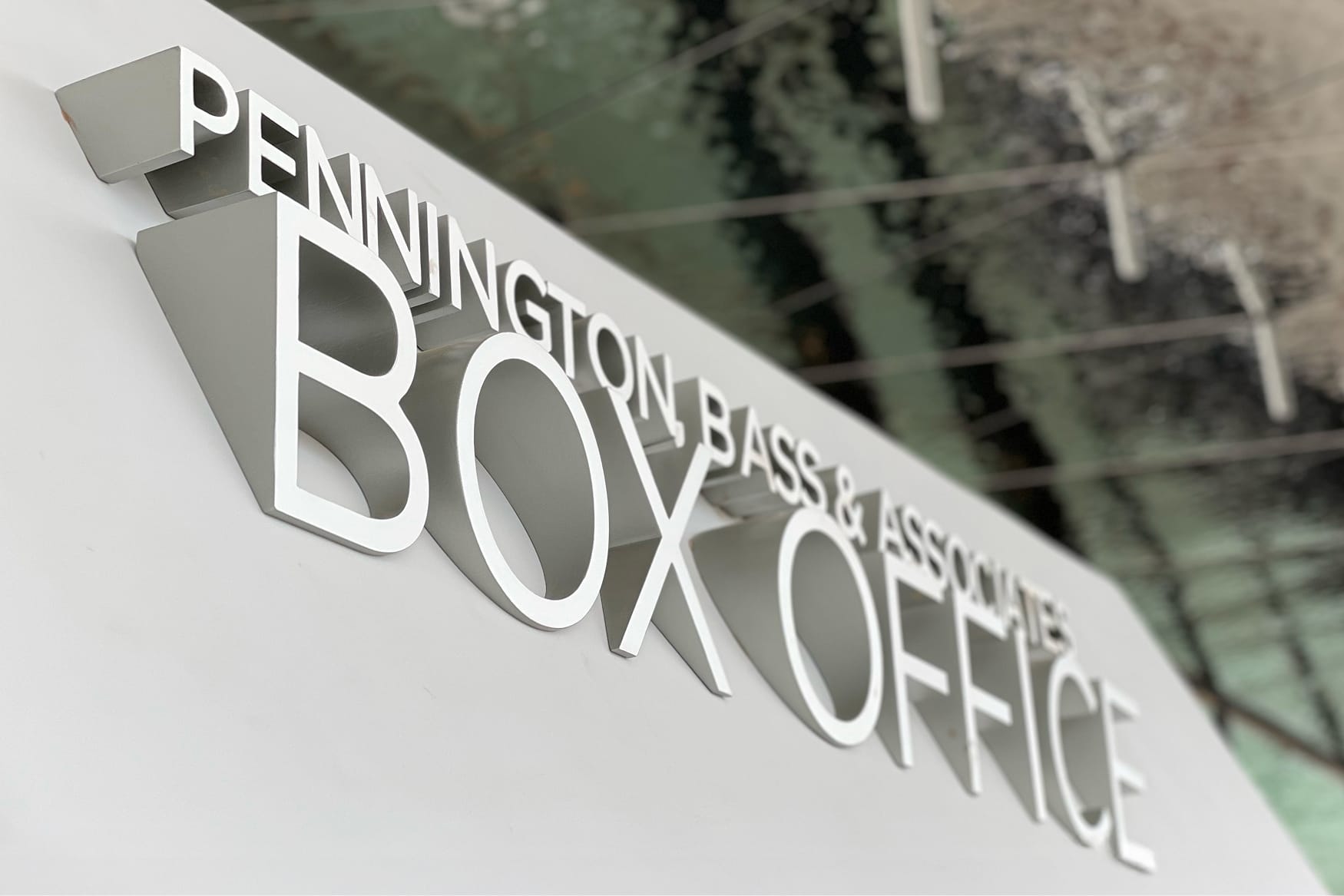 Dimensional brushed silver donor-named box office signage reading "Pennington Bass & Associates Box Office" mounted on a white angled wall at Buddy Holly Hall of Performing Arts and Sciences, Lubbock Texas
