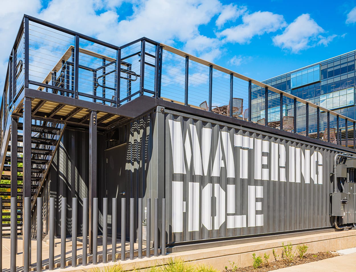 "Watering Hole" large-format tenant identification signage and experiential graphics applied to a repurposed shipping container bar structure at Toyota Music Factory mixed-use entertainment district in Irving, Texas — RSM Design branded environments, specialty graphics, and experiential placemaking for mixed-use, food and beverage, and streetscape destinations.
