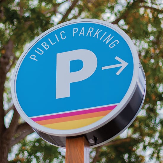 Round blue "Public Parking" directional sign with a colorful sunset stripe accent in Dana Point - environmental graphic design by RSM Design