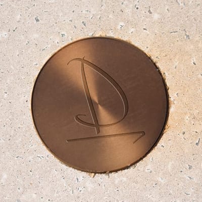 A custom-engraved bronze marker embeds the project’s identity directly into the ground plane, offering a subtle yet enduring expression of place.