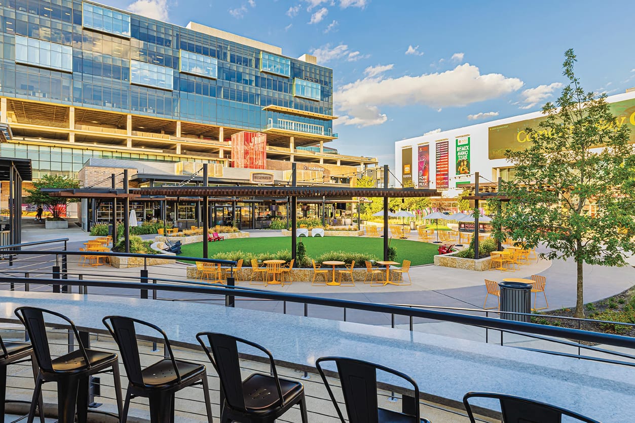 Elevated terrace overlooking an activated public plaza at Toyota Music Factory mixed-use entertainment district in Irving, Texas, featuring large-format event banners, branded environmental signage, and experiential graphics — RSM Design placemaking, print and digital collateral, wayfinding and signage design for mixed-use, food and beverage, retail, and sports and entertainment destinations.
